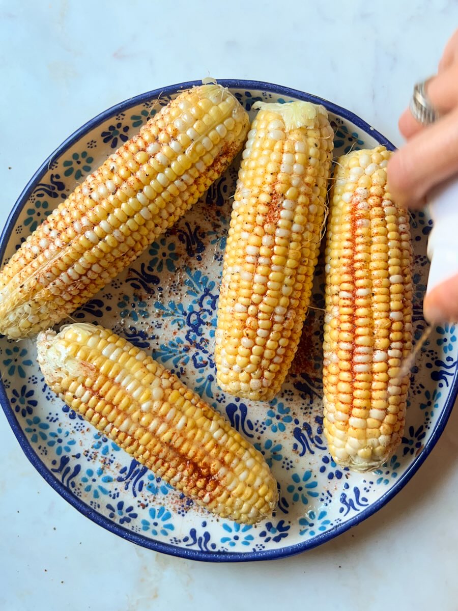 Ninja air fryer corn on the cob, spray seasoned corn with oil.