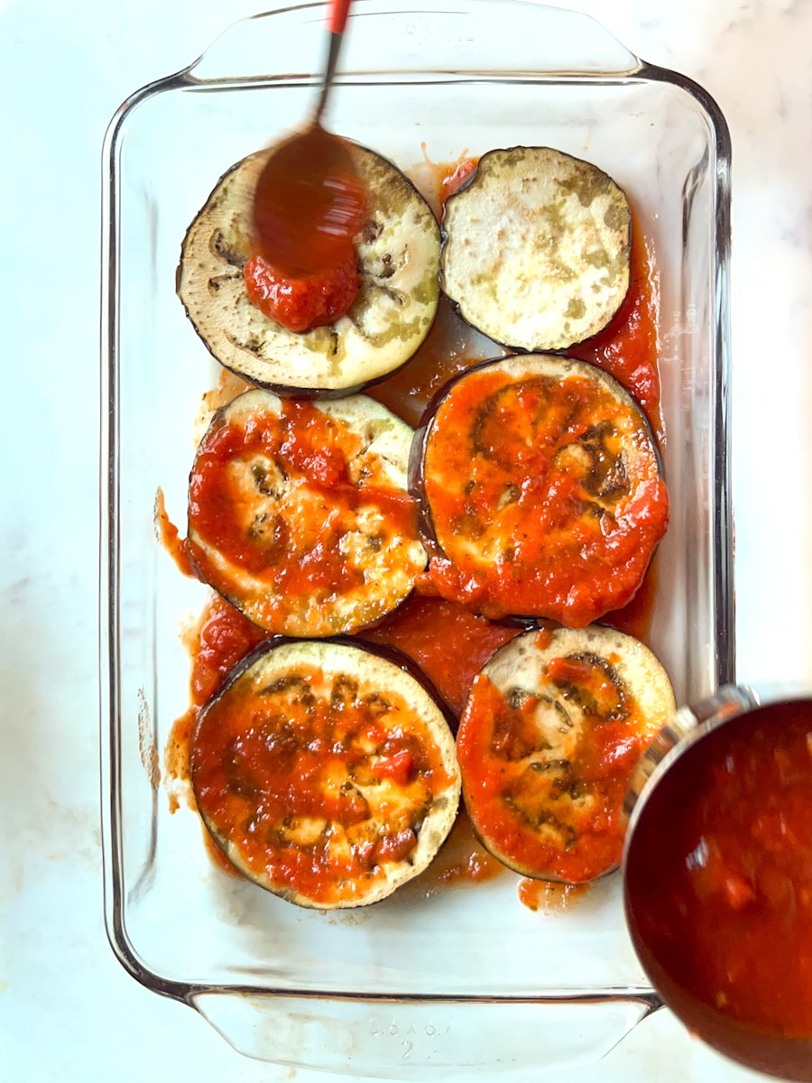 Baked cheesy eggplant, spoon tomato sauce over eggplant slices