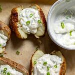 Oven baked potato with sour cream and green onion served on a baking sheet