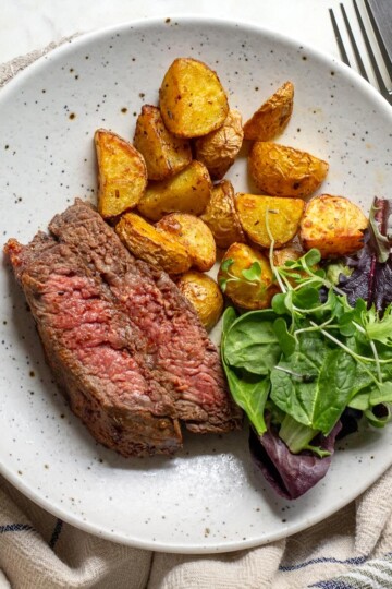 A plate with sliced air fryer steak, crispy baby potatoes, and a fresh side salad.