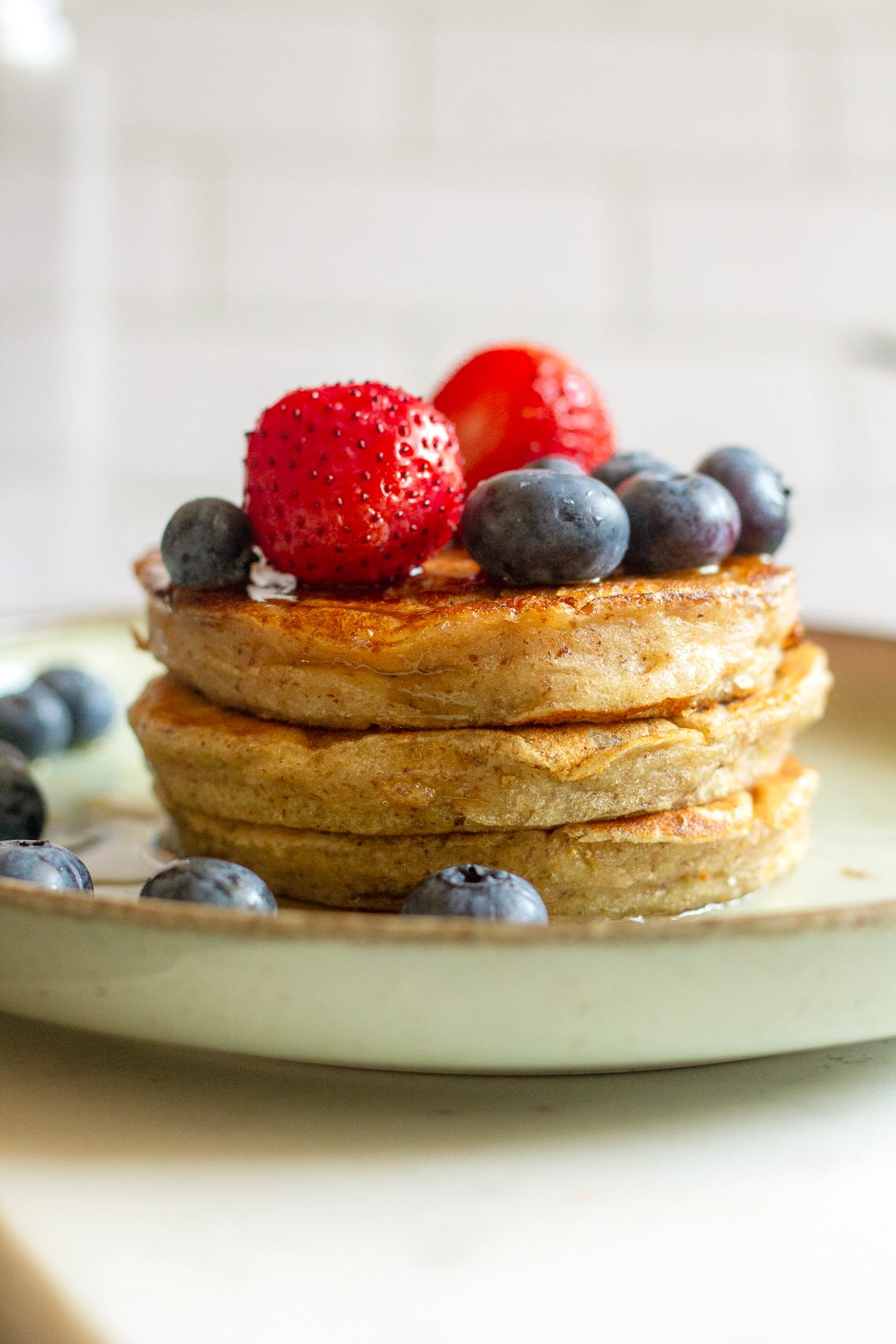 Banana pancakes with maple syrup, strawberries and blueberries served on a plate.