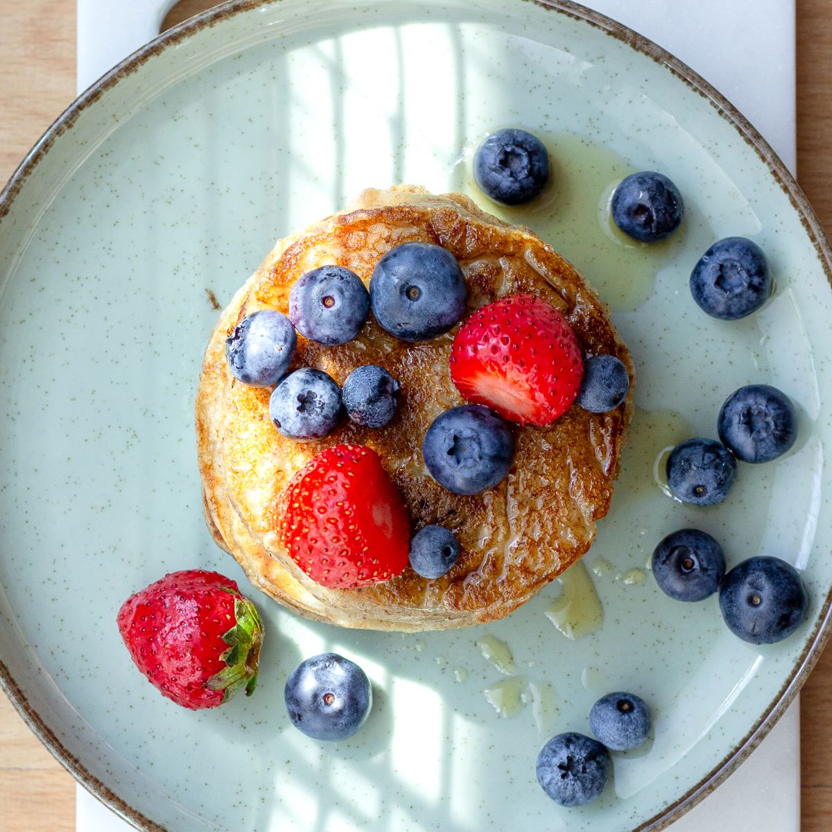 Banana pancakes with maple syrup, strawberries and blueberries on a plate.