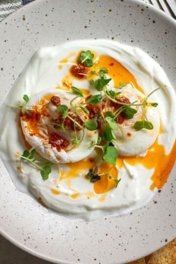 Close-up of perfectly poached eggs on a Greek yogurt base, garnished with microgreens and served with toasted bread.