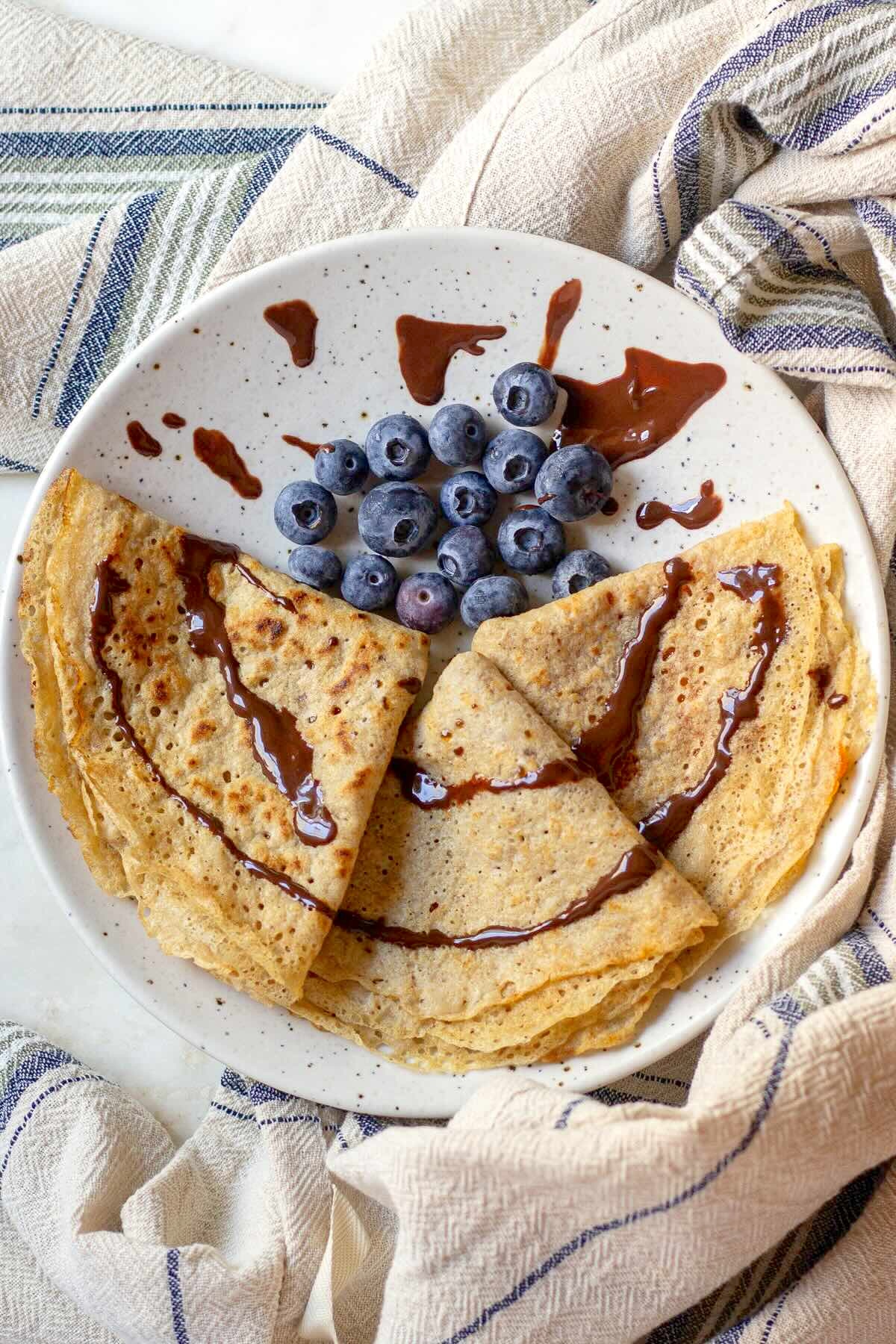 Whole-wheat crepes served on a plate with blueberries and chocolate