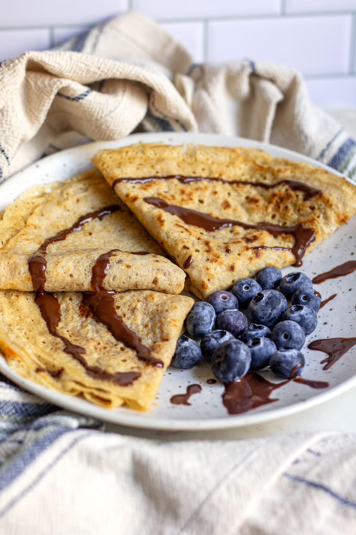 Whole-wheat crepes served on a plate with blueberries and chocolate syrup
