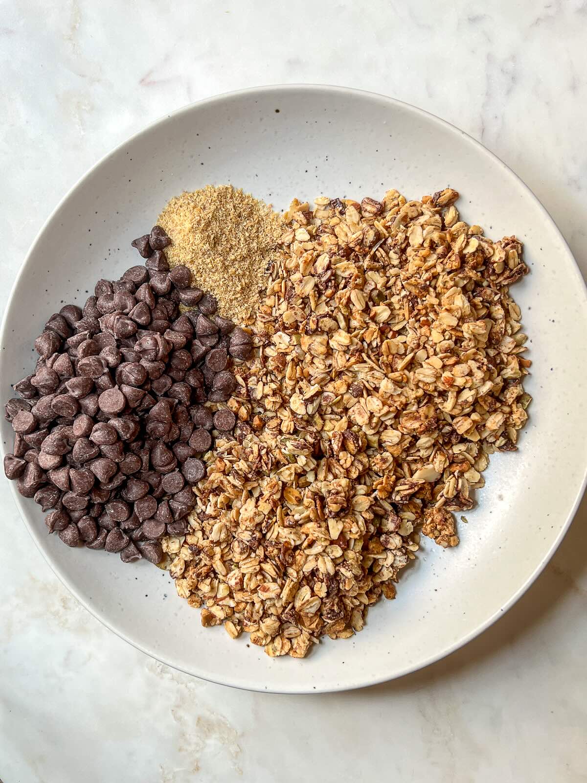 Dry ingredients for homemade granola bars without peanut butter, including granola, ground flaxseed, and chocolate chips, measured and ready in a mixing bowl.
