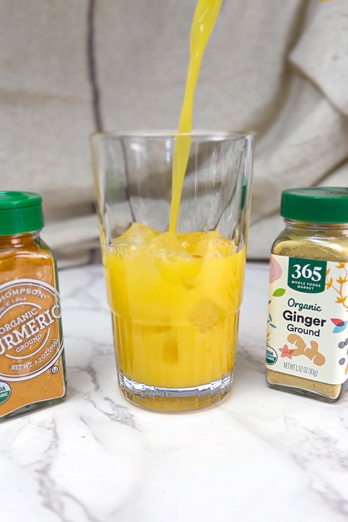 Morning meditation juice preparation, adding the mixture of orange juice and ginger and turmeric over ice cubes.
