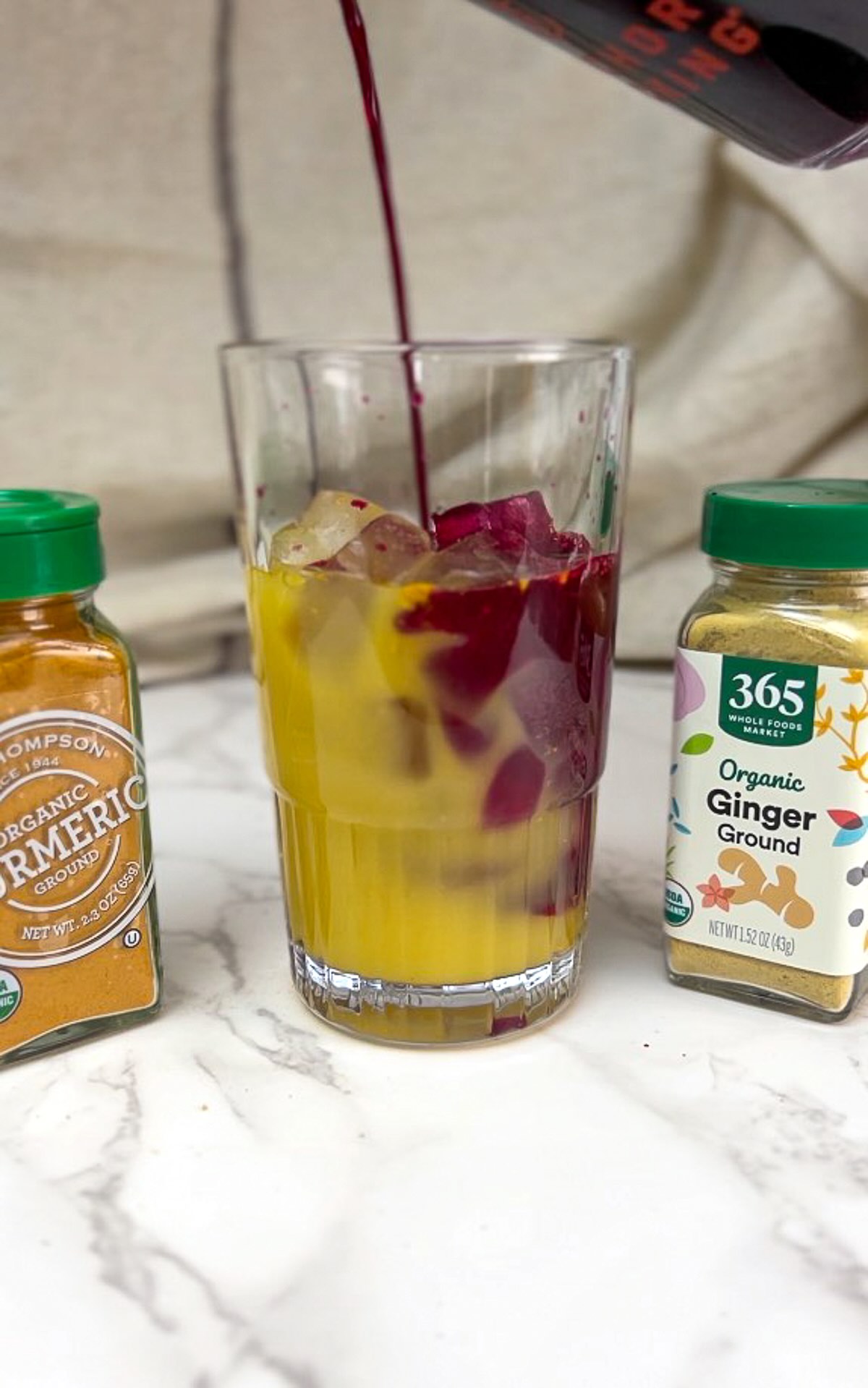 Morning meditation juice preparation, adding beet juice to a mix of orange juice and ginger and turmeric over ice in a tall glass.