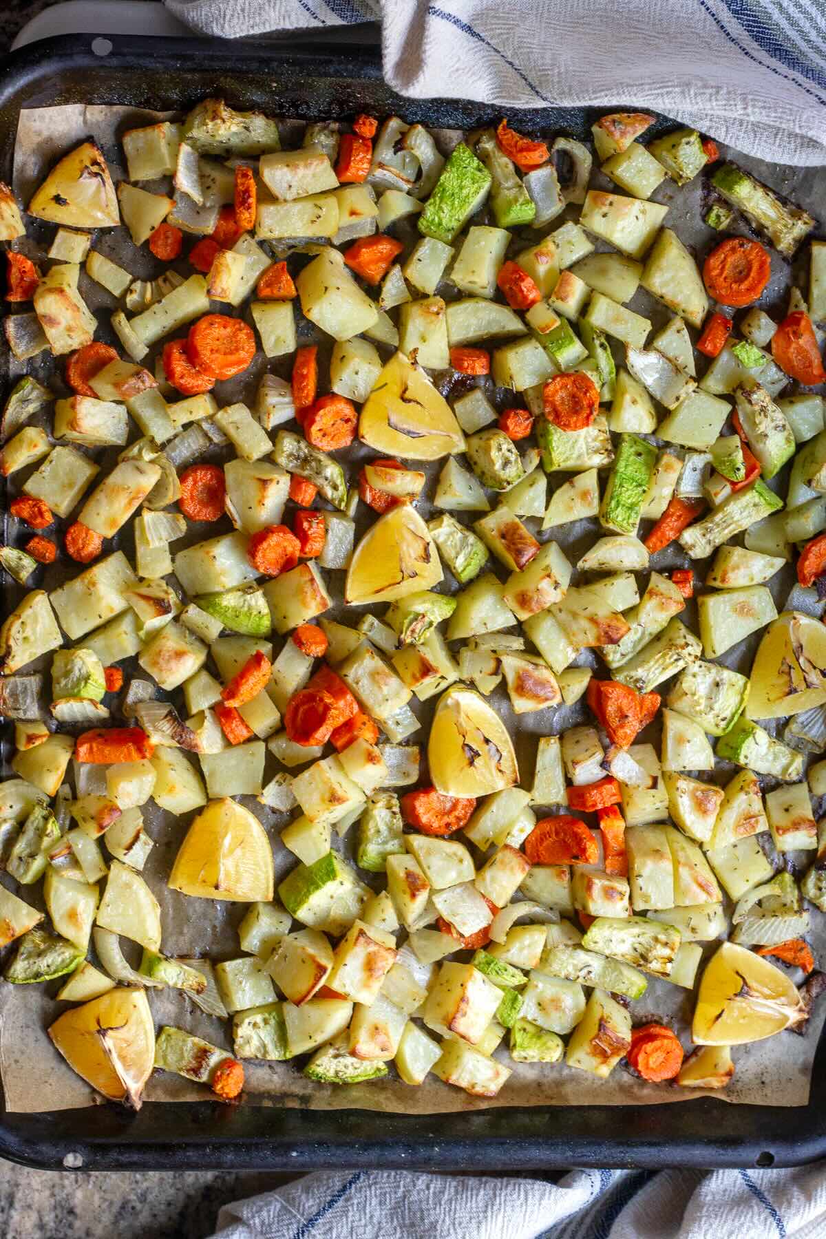 Oven roasted potatoes and carrots with onion and zucchini shown in the baking pan.