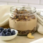 Close-up of vegan cheesecake in a jar with date-granola crumb crust and cashew filling
