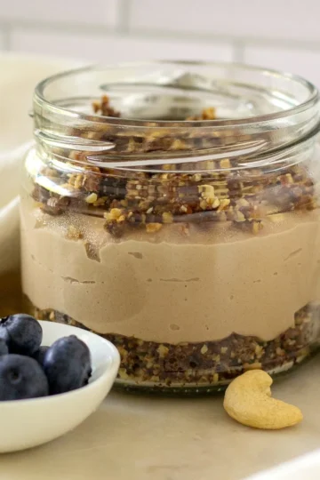 Close-up of vegan cheesecake in a jar with date-granola crumb crust and cashew filling